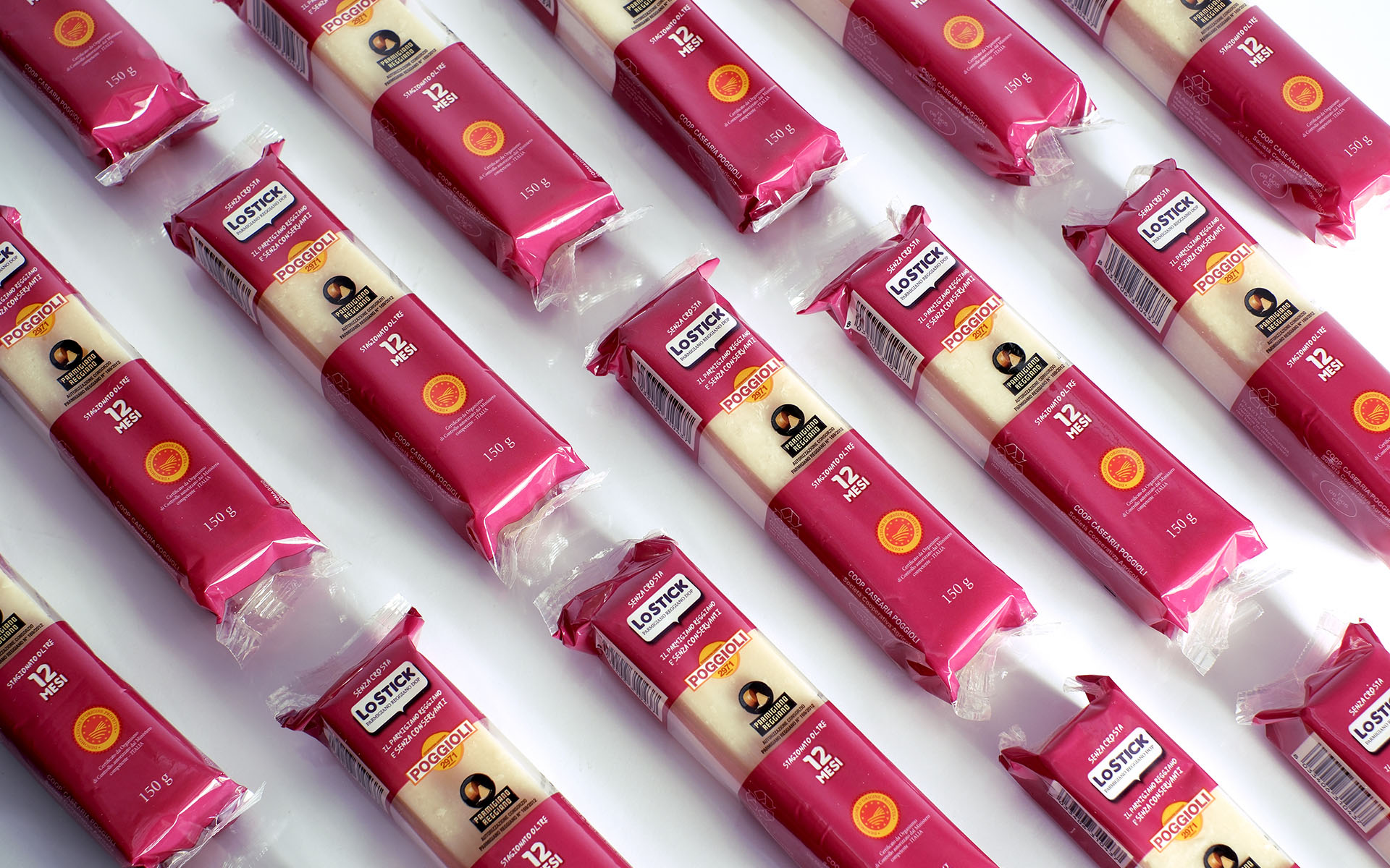 L’immagine mostra una disposizione ordinata e ripetuta di numerose confezioni di uno snack chiamato “LOSTICK Parmigiano Reggiano” su uno sfondo bianco. Le confezioni sono disposte in file oblique e parallele che riempiono interamente tutto lo spazio visivo: sono tutte orientate nello stesso modo, perfettamente allineate, generando un effetto visivo di pattern regolare e ritmico. Ogni confezione è rettangolare, lunga e sottile, realizzata in plastica e protetta da un involucro dal colore predominante fucsia o magenta vivo. Entrambe le estremità della confezione sono fucsia, con la parte centrale trasparente che lascia intravedere il bastoncino chiaro di Parmigiano Reggiano all’interno, dal colore crema pallido e texture compatta. Sulla confezione, in alto, c’è una piccola etichetta bianca con il bordo fucsia su cui si legge in nero “SENZA CROSTA”. Subito sotto si trova la scritta “LOSTICK” riportata in blu e in grande su uno sfondo bianco, seguita dalla scritta in lettere maiuscole gialle e arancioni “POGGIOLI” e dal logo, costituito da un cerchio arancione sfumato con una stilizzazione grafica. Al centro, spicca il simbolo ufficiale di Parmigiano Reggiano DOP (Denominazione di Origine Protetta), in nero e oro, accompagnato da una scritta che garantisce l’autenticità del formaggio. Poco più in basso, su uno sfondo fucsia, campeggia l’indicazione “stagionatura oltre 12 MESI”, con il numero “12” scritto in bianco molto grande. Verso la base della confezione, ci sono le informazioni sul peso netto: “150 g”. Nel quadrante inferiore destro di ciascuna confezione, è stampato il marchio di qualità DOP, rappresentato da un cerchio con una corona di spighe oro e rosse. La plastica trasparente che avvolge il formaggio lascia intravedere la consistenza tipica e leggermente granulosa del Parmigiano stagionato. Le confezioni sono tutte sigillate ermeticamente e presentano pieghe ordinate dove la plastica è stata chiusa alle estremità. La luce nella foto è chiara e uniforme, senza ombre marcate: mette in risalto l’ordine e la brillantezza dei colori delle confezioni, esaltando l’aspetto igienico e fresco dei prodotti. Nessun elemento di distrazione sullo sfondo, solo bianco puro. **Sintesi sensoriale:** L’immagine trasmette una forte sensazione di ordine, pulizia ed efficienza, con una nota di vivacità data dal colore fucsia molto acceso del packaging. L’effetto ripetuto e regolare delle confezioni suggerisce modernità, praticità e anche abbondanza, come a comunicare la disponibilità di uno snack salato sano e facile da trasportare ovunque. La grafica della confezione è chiara, moderna e facilmente leggibile, con una comunicazione visiva incentrata sulle qualità di autenticità, qualità certificata e praticità.